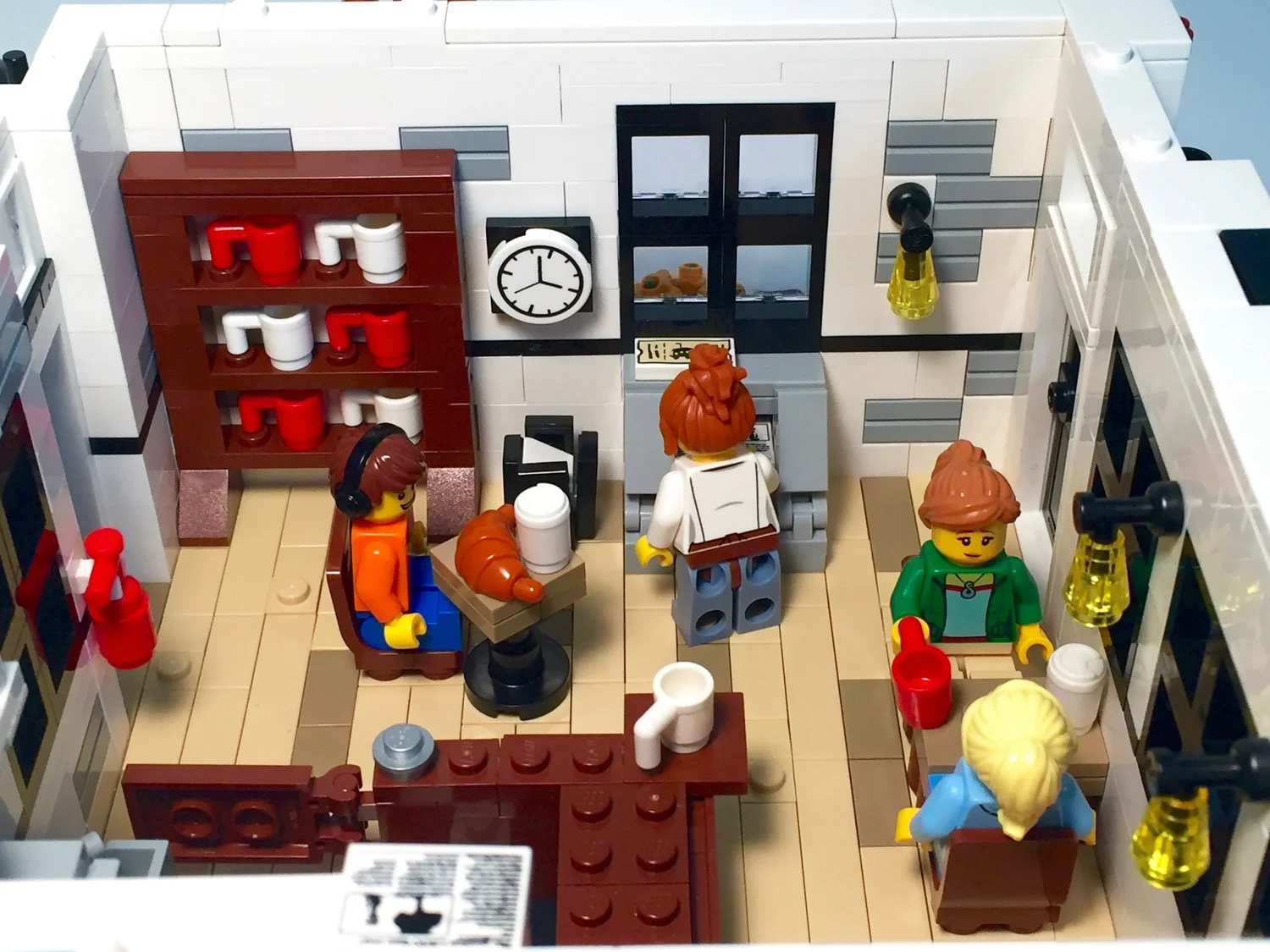 Interior corner of the LEGO café with a mug shelf, clock, newspaper stand and minifigures