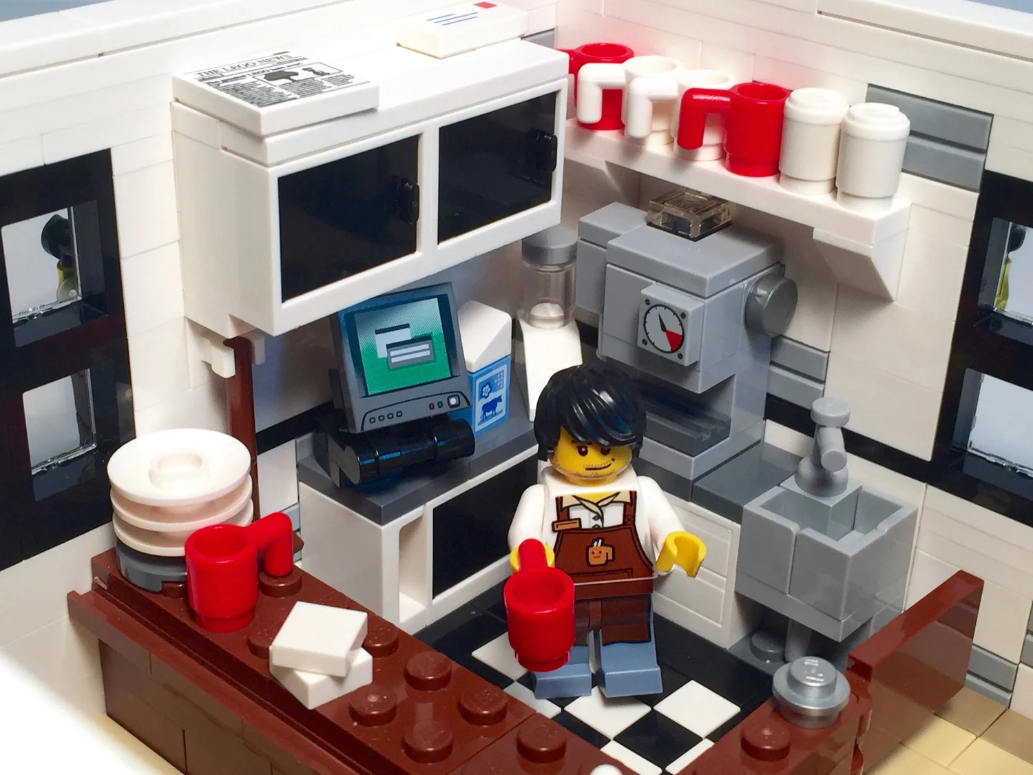 Close-up of the café service area with espresso maker, cash register, shelves of mugs and a barista minifigure