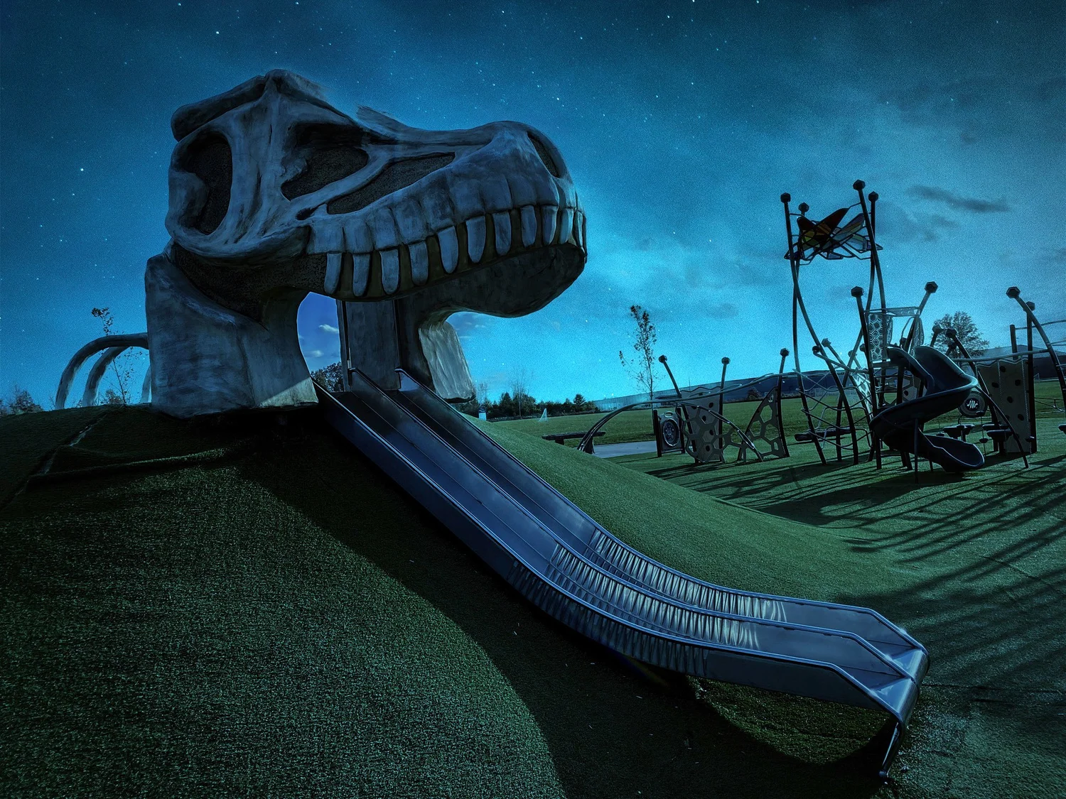 Playground slide built into a giant dinosaur skull under a starry dusk sky