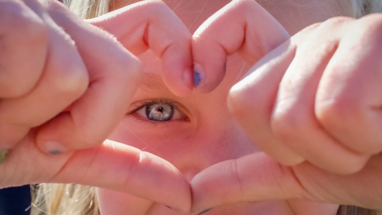 Two hands forming a heart shape that frames a child's eye