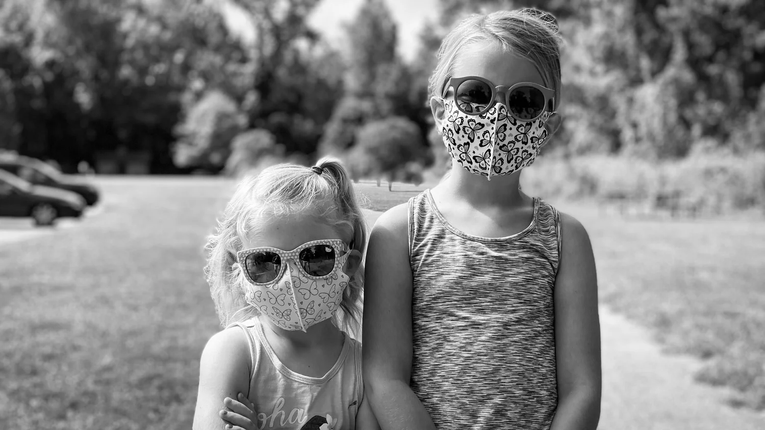 Black and white portrait of two kids in butterfly-print masks and sunglasses